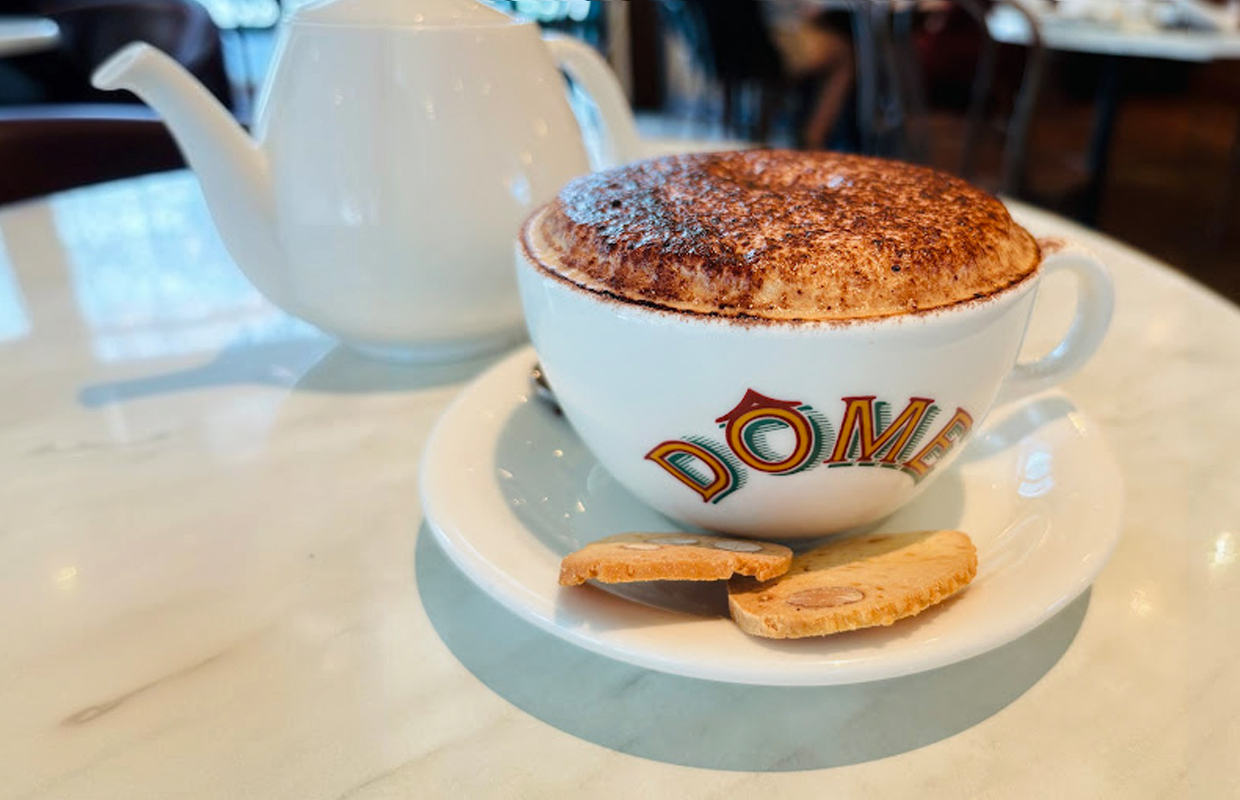 slides-5 DÔME white coffee cup of cappuccino with some biscuit on top of white table in DÔME cafe